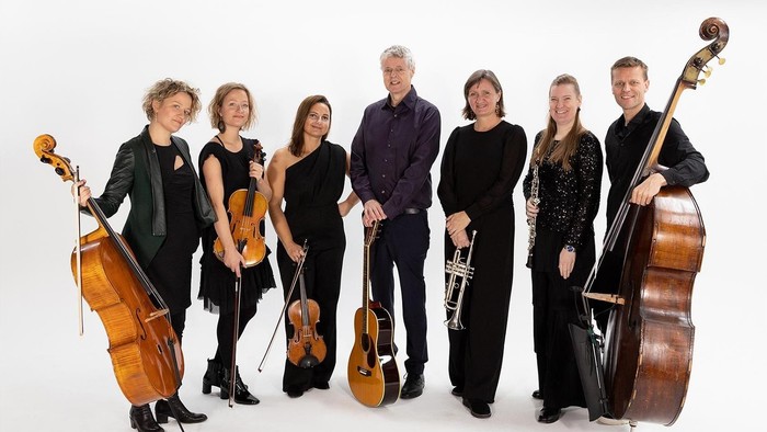 En stryger- og messingensemble på syv musikere, der poserer sammen med deres instrumenter.