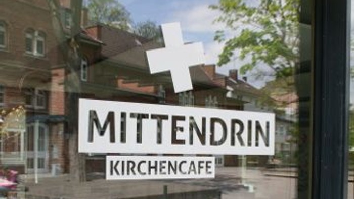 Das Schaufenster der Kirchencafé Mittendrin zeigt ein weißes Kreuz und den Namen des Cafés.