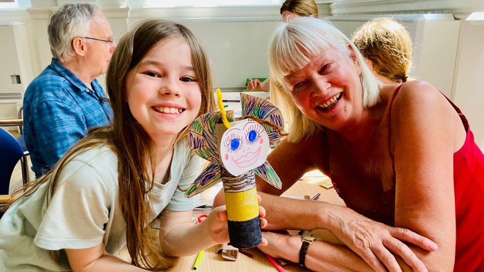 A young girl and an older woman smile while crafting puppets at a table.