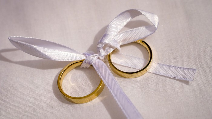 Zwei goldene Ringe, die mit einem weißen Satinband zusammengebunden sind, auf einem weichen Stoffhintergrund.