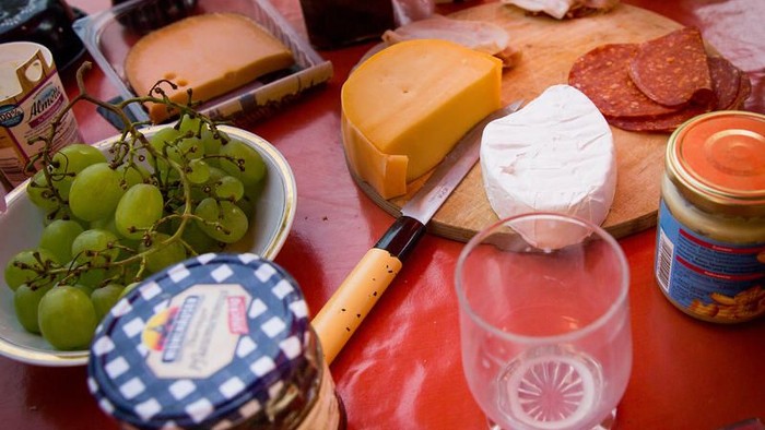 Der Tisch ist mit verschiedenen Käsesorten, Trauben, Wurst, Marmelade und Getränken beladen.