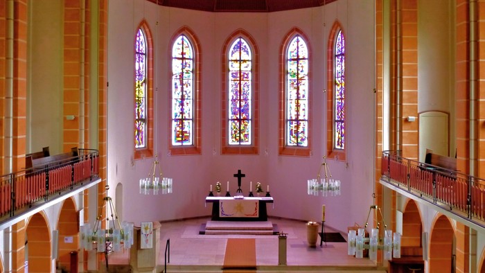 Innenraum einer Kirche mit Altarraum und farbigen Fenstern