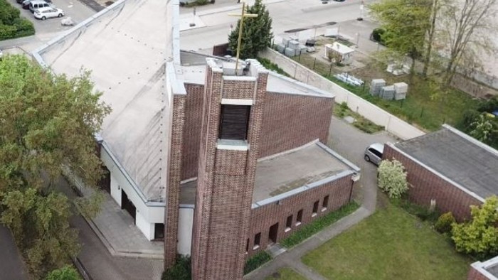 Das Bild zeigt eine Kirche mit hohem Turm und umgebenden Gebäuden und Autos.