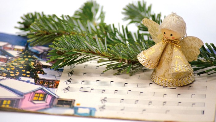 Ein goldener Engel sitzt auf Notenblättern neben einem Tannenzweig