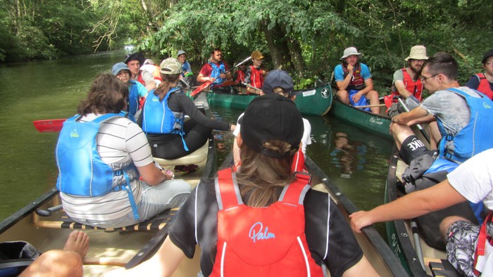 Eine Gruppe von Menschen in Kanus auf einem Fluss, umgeben von Grün.