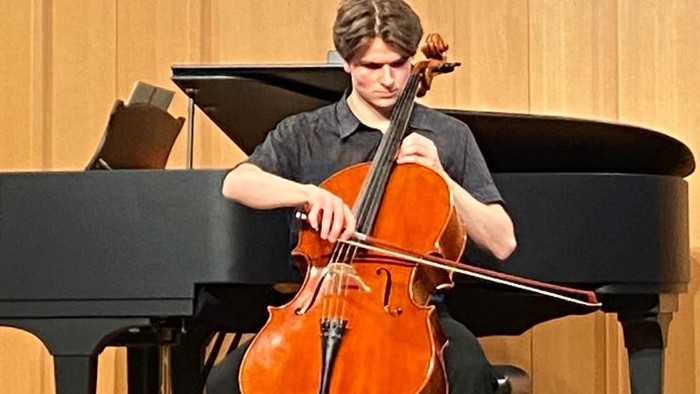 Junger Mann spielt Cello im Konzertsaal vor einem Flügel