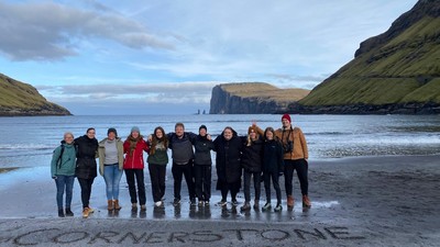 En gruppe af mennesker står sammen på en strand med et bjerg i baggrunden