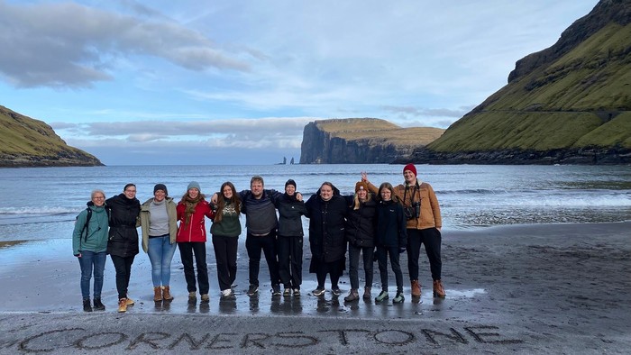 En gruppe af mennesker står sammen på en strand med et bjerg i baggrunden