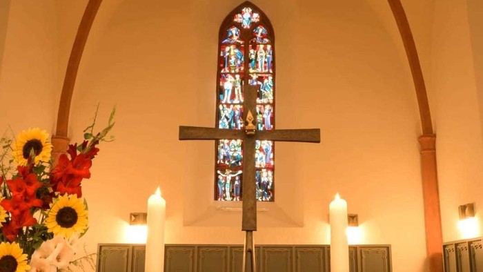 In der Kirche: Altar mit Kreuz, Kerzen und Blumen vor buntem Fenster