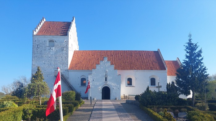 Historisk hvid kirke med røde teglstenstag og en flagstang med et skandinavisk flag.