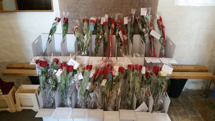 Forskellige buketter af røde roser indpakket i plastik og mærket, udstillet på træhylder.