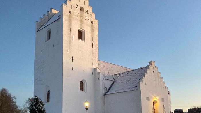 En snede hvid kirke med tårn og en lystet indgang i snedæknede omgivelser