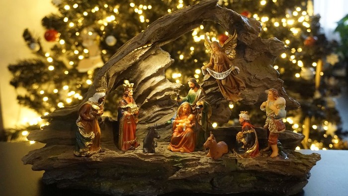 Eine Weihnachtskrippe mit Figuren vor einem beleuchteten Christbaum.