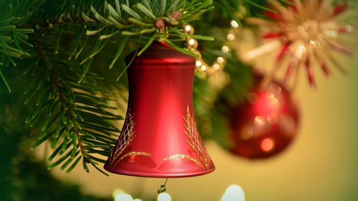 Ein roter Weihnachtsglocken-Schmuck hängt an einem Tannenbaum.