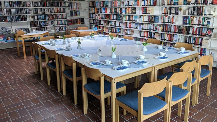 Ein langer Tisch in einer Bibliothek mit weißen Tischdecken, Teetassen und Stühlen.