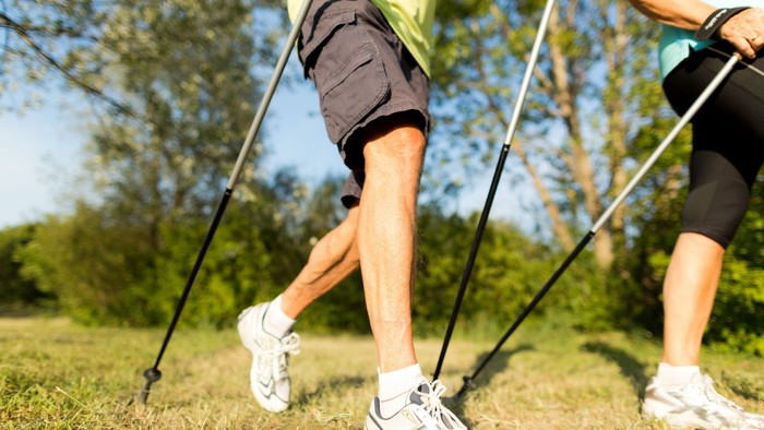 Zwei Personen gehen mit Nordic Walking Stöcken durch einen Park