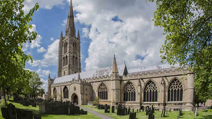 Large Gothic-style church with tall spires and stained glass windows, surrounded by a cemetery and trees under a partly cloudy sky.
