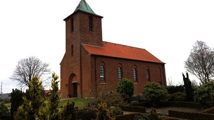En rød murstenskirke med spiret og klokketårn.