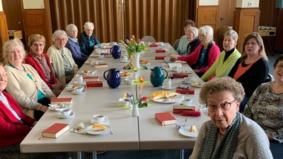 Gruppe älterer Menschen versammelt sich fröhlich um einen langen Tisch zu einer Mahlzeit oder einem Treffen.