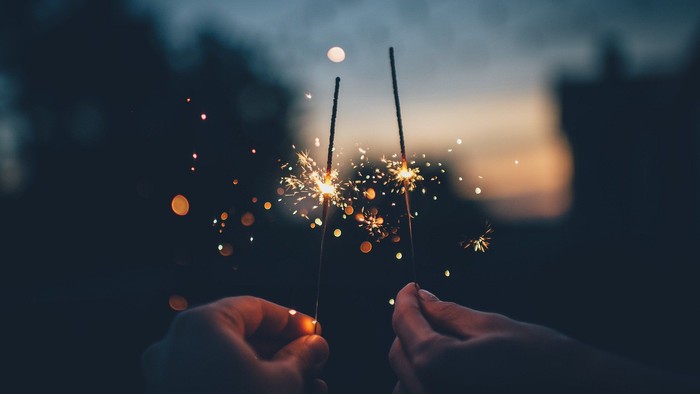 Zwei Hände halten ein Feuerwerk, das in der Dämmerung leuchtet