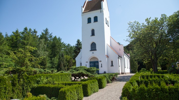 En hvid kirke med tårn og omgivet af grønne buske og træer