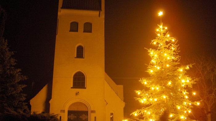 En lyssende juletree foran en belyset kirke