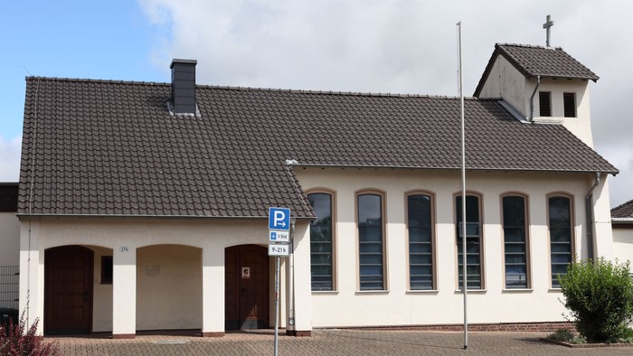 Kleine Kirche mit schwarzem Dach und weißer Fassade, daneben Parkplatz-Schild