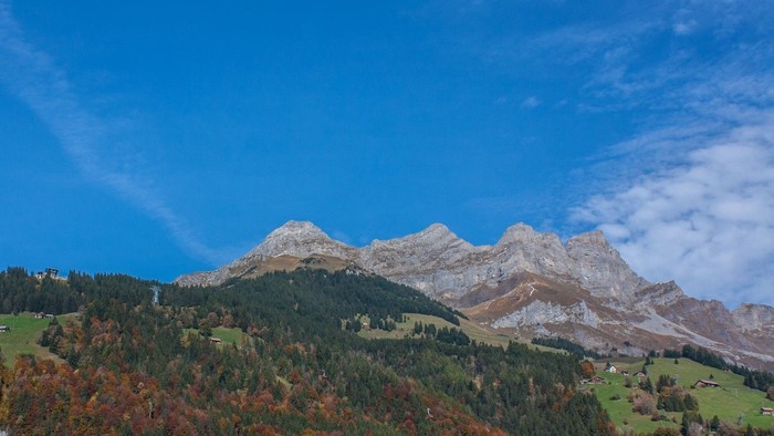 Majestätische Berge mit herbstlichen Wäldern unter einem klaren, leuchtend blauen Himmel.