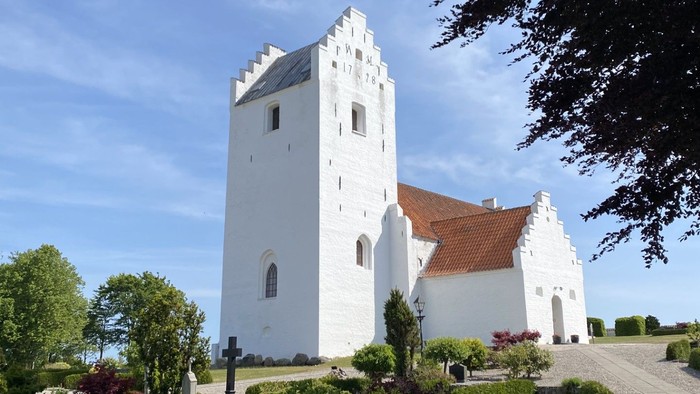 Et hvidt kloster med tårn og røde tag i en træket garden
