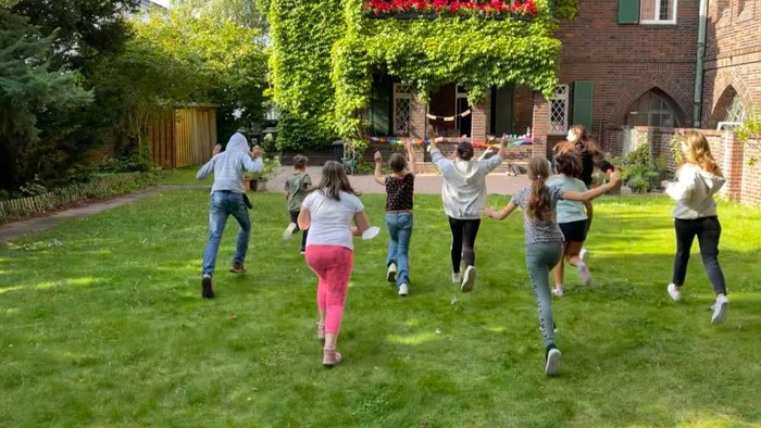 Eine Gruppe von Menschen tanzt auf einem grasbewachsenen Bereich vor einem Haus.