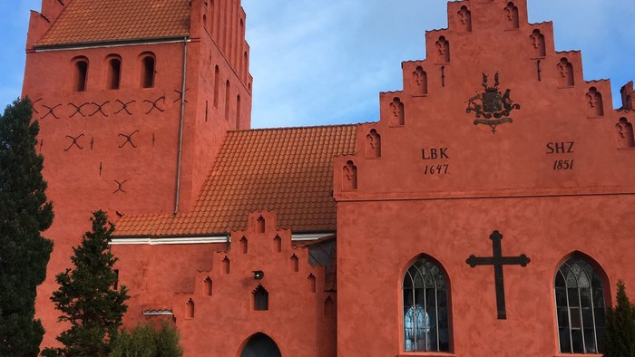 Røde kirke med tårn og gravsteder i forgrunden