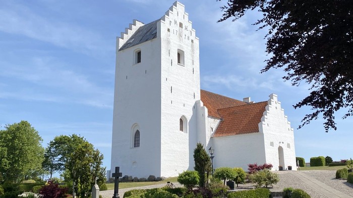 Et hvidt kloster med tårn og røde tag i en træket garden