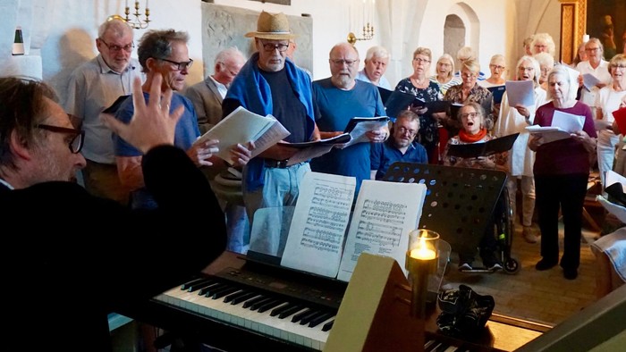 En kirkekor, hvor en mand spiller orgel mens koret synger.