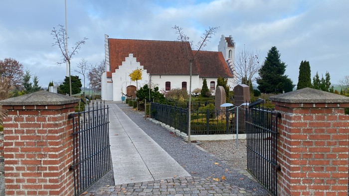 En smuk kirke med røde tag og hvidt udseende, omgivet af en mur og en sti.