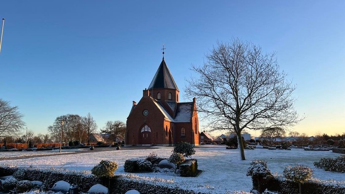 En rød kirke i sneklædt landskab ved solopgang
