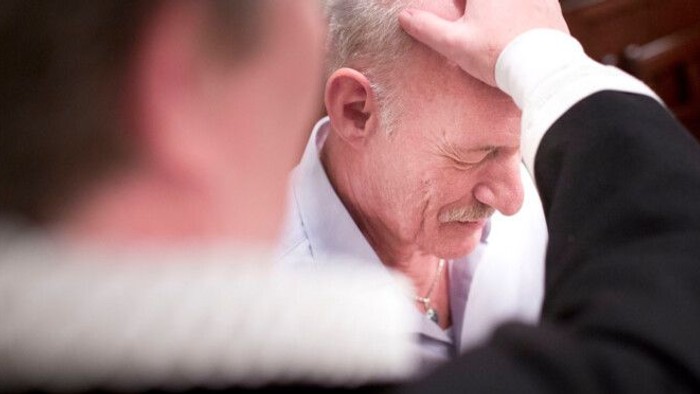 En mand med hånden på hovedet ser ud til at hvile eller bede i en overfyldt omgivelse.