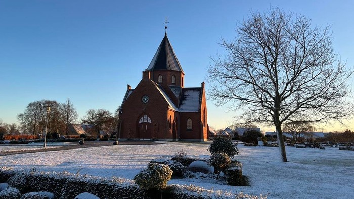 En rød kirke med spiret og klokke i en snedækked park