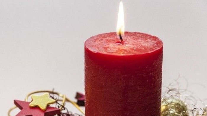 Eine rote Kerze steht auf einem Beet mit Tannenzweigen und Weihnachtsdekorationen.