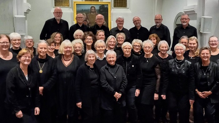 Gruppe af mennesker, der poser sammen i sort påklædning, sandsynligvis til et kor eller en opvisning.