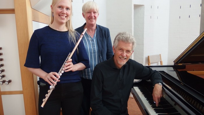 Tre personer poserer sammen, en med en fløjte og en anden ved et klaver.
