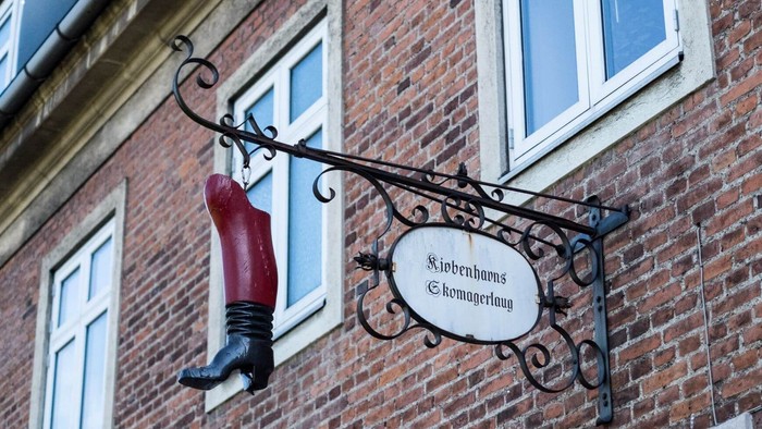En rød sko hænger ved et skilt på et murstenshus