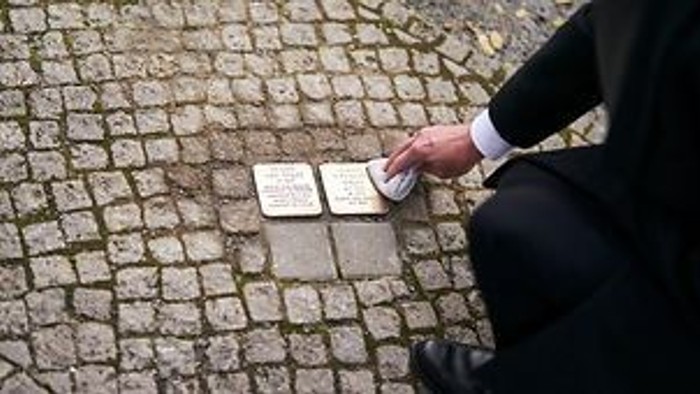 Mann in Anzug beugt sich auf Kopfsteinpflaster, um etwas auf dem Boden zu inspizieren.