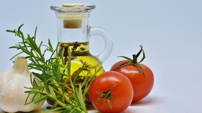 Das Bild zeigt eine Glasflasche mit Öl, Knoblauch, Rosmarin und Tomaten