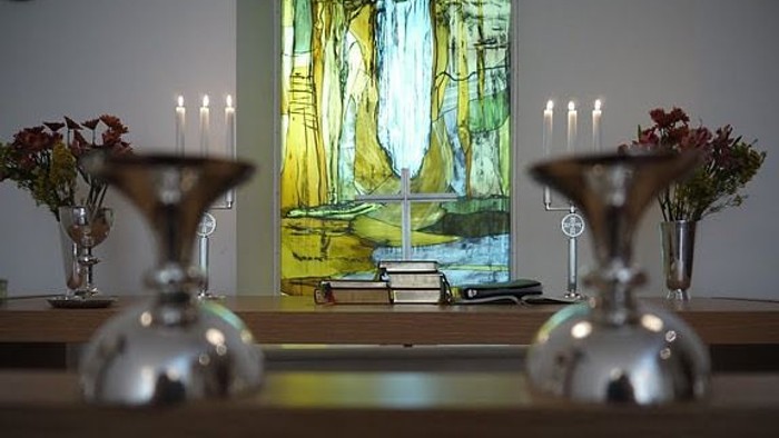 To bordsmidter med lyse candlesticks og blomsterarrangeringer foran et maleri