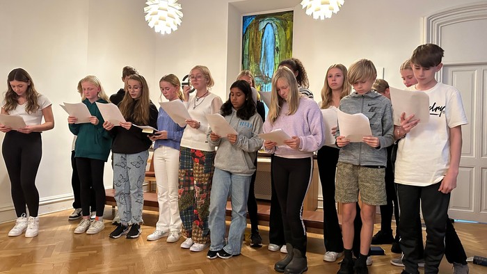 En gruppe unge står i en sal og synger fra noter.