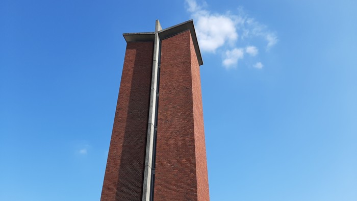 En høj røde tegltårn mod et blødt blå himmel.