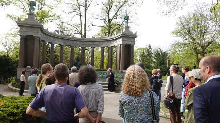 Eine Gruppe von Menschen versammelt sich vor einem großen Torbogen in einem Park.