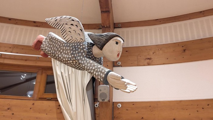 Verspielte Marionettenfigur, die mit ausgebreiteten Armen und einem lächelnden Gesicht von der Decke hängt.