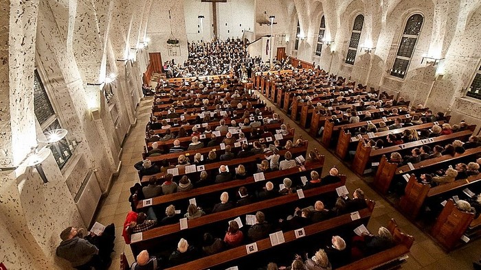 Große Kirche mit vielen Gläubigen in Reihen sitzend, ein Kreuz und ein Altar sind sichtbar