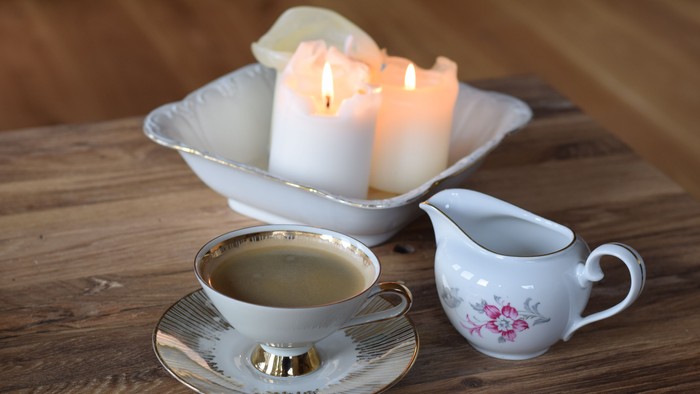 Ein Holztisch mit einer Teetasse, Milchkännchen und brennenden Kerzen in einer Schale